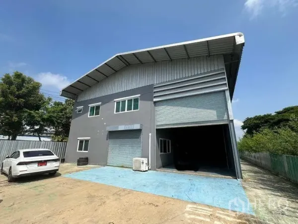 Warehouse for rent in Pathum Thani - Front exterior of metal-roof warehouse with two roller shutters, loading apron and parking in Lam Luk Ka.
