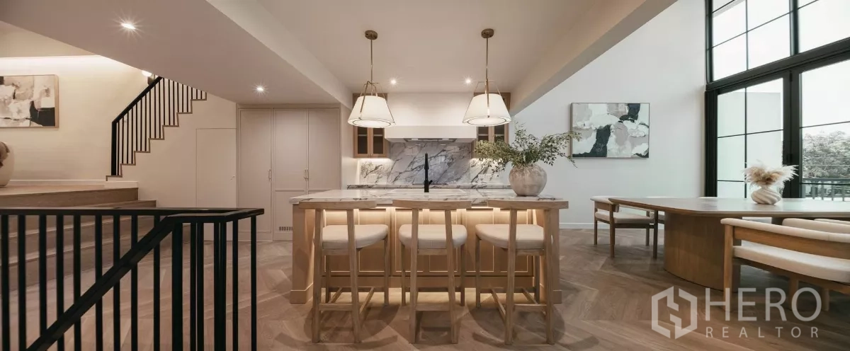 Townhouse for rent in Watthana, Bangkok - Front view of marble island kitchen and dining table beside floor-to-ceiling windows.