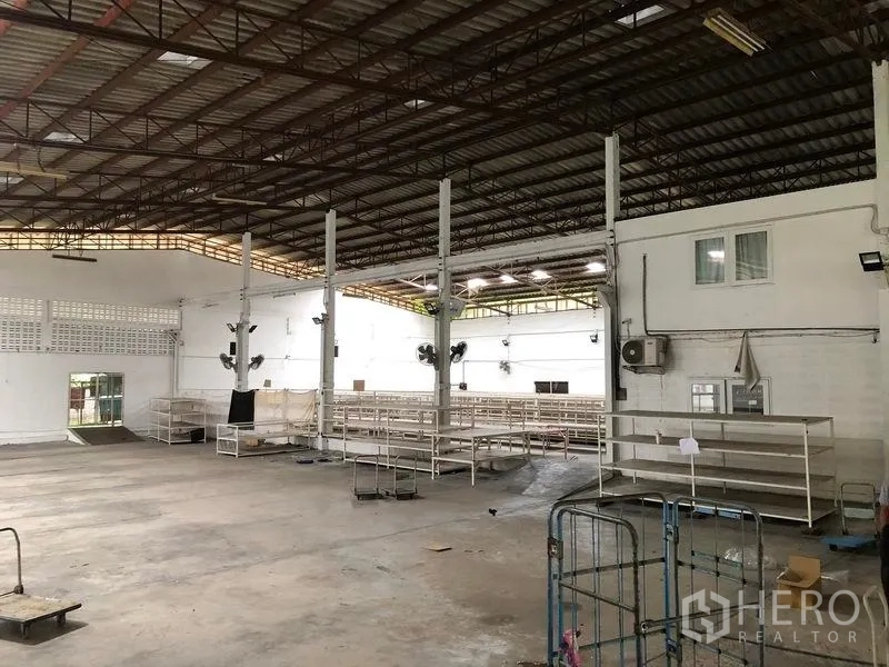 Warehouse for rent in Bang Kapi, Bangkok - Open-plan warehouse with shelving, wall fans and a small office section.