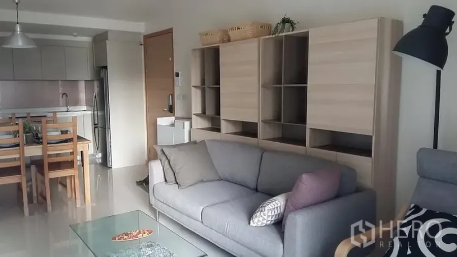Condominium for rent in Watthana, Bangkok - Open-plan living room with grey sofa, wall shelving, and modern kitchen in a Bangkok condo.