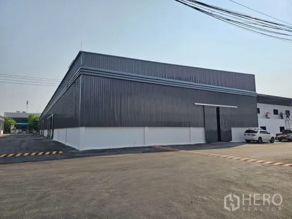 Warehouse for rent in Khlong Toei, Bangkok - Corner exterior of metal-panel warehouse featuring a large sliding door and parking area.