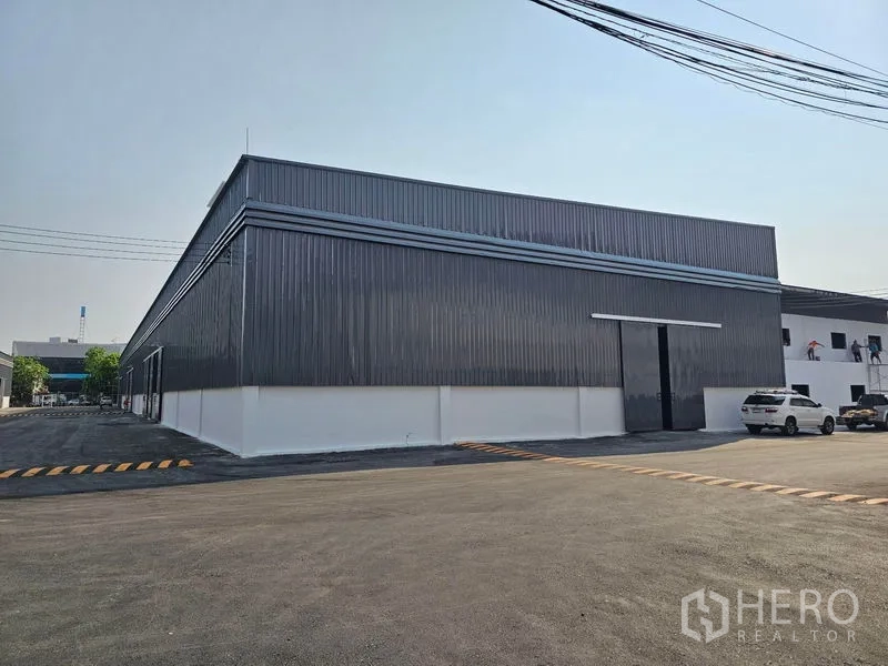 Warehouse for rent in Khlong Toei, Bangkok - Corner exterior of metal-panel warehouse featuring a large sliding door and parking area.