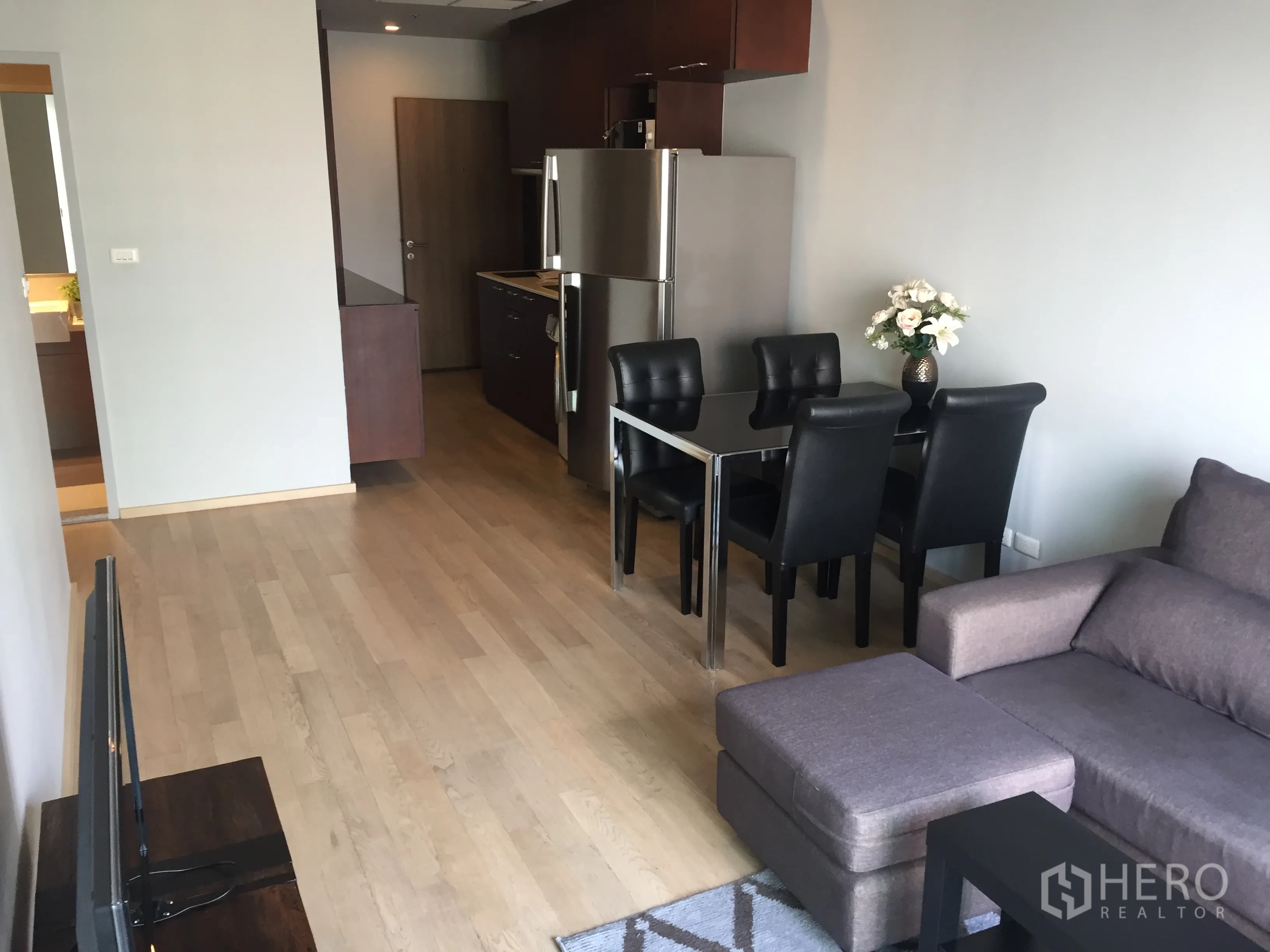 Condominium for rent in Bangkok - Open-plan living and dining area with light wood floors, grey sofa, and a black glass dining table.