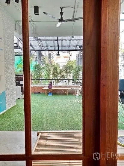 Shophouse for rent in Pathum Wan, Bangkok - View through wooden framing to a covered outdoor area with turf, ceiling fans and greenery.