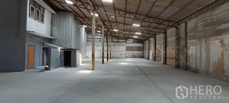 Warehouse for rent in Phra Khanong, Bangkok - Interior view showing office and service rooms, column guards, and a high roof with skylights for natural light.