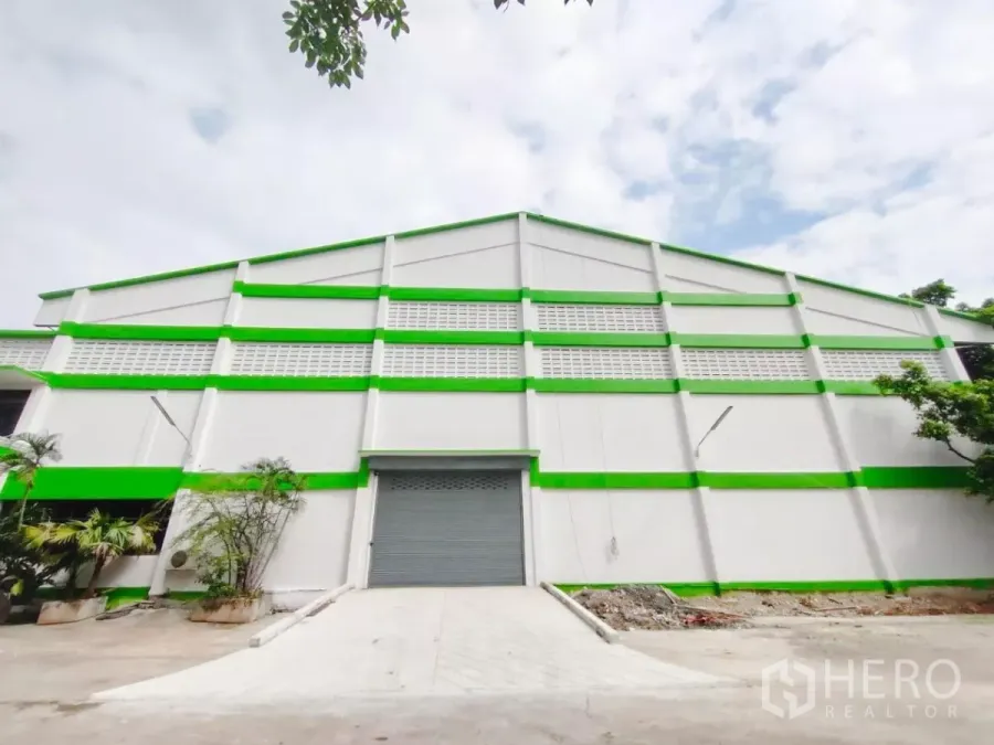 Factory for sale in Samut Prakan - Green-and-white factory facade with roller shutter door and loading ramp in Bang Sao Thong, Samut Prakan.