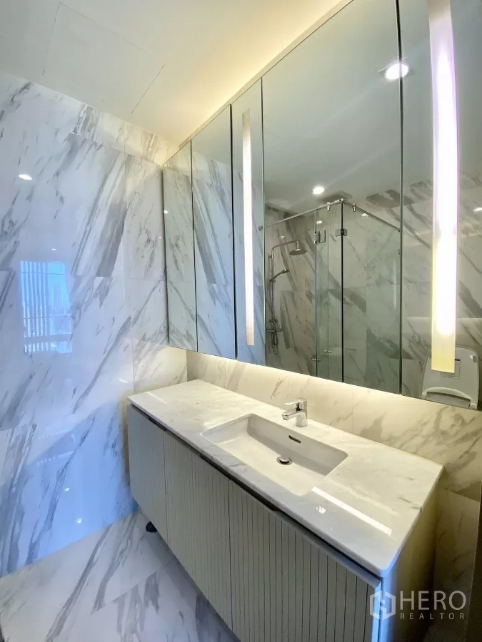 Condominium for sale in Pathum Wan, Bangkok - Marble-clad bathroom with backlit mirror and sleek vanity sink.
