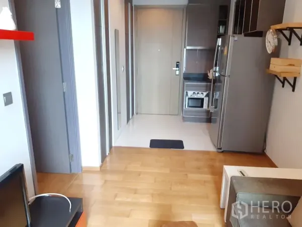 Condominium for rent in Khlong Toei, Bangkok - View toward the entry showing wooden floors, built-in kitchen with stove and fridge, hallway storage and shelving.