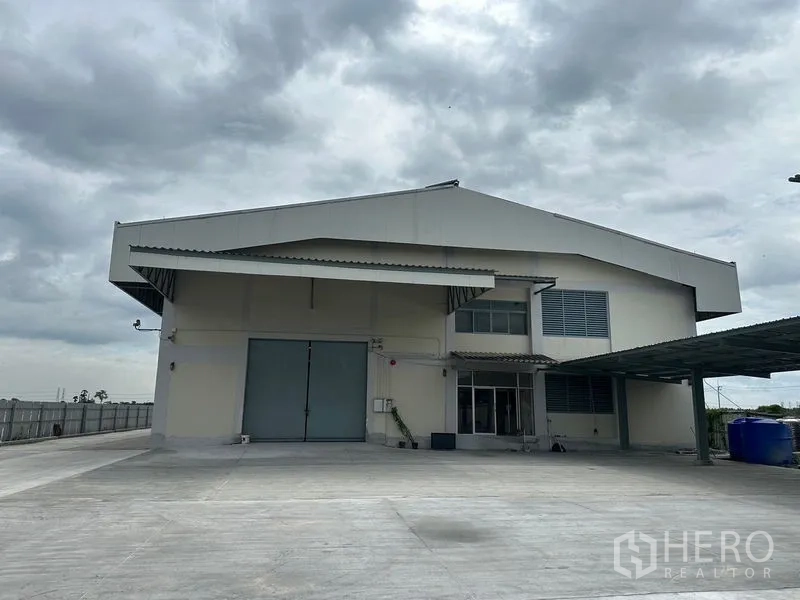 Factory for rent in Lam Luk Ka, Pathum Thani - Long side elevation with covered walkway and multiple loading doors along the driveway.