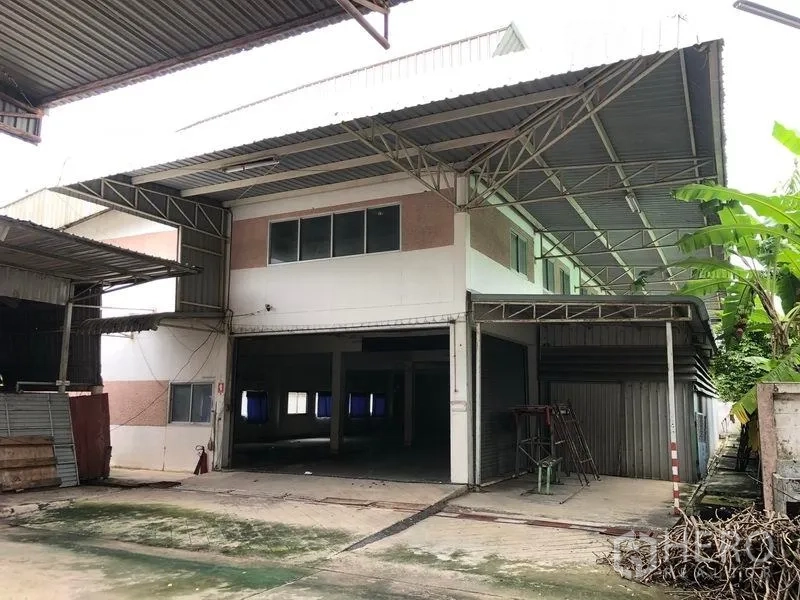 Factory for sale in Lam Luk Ka, Pathum Thani - Covered loading bay with roller shutters beside a two-storey administrative building.