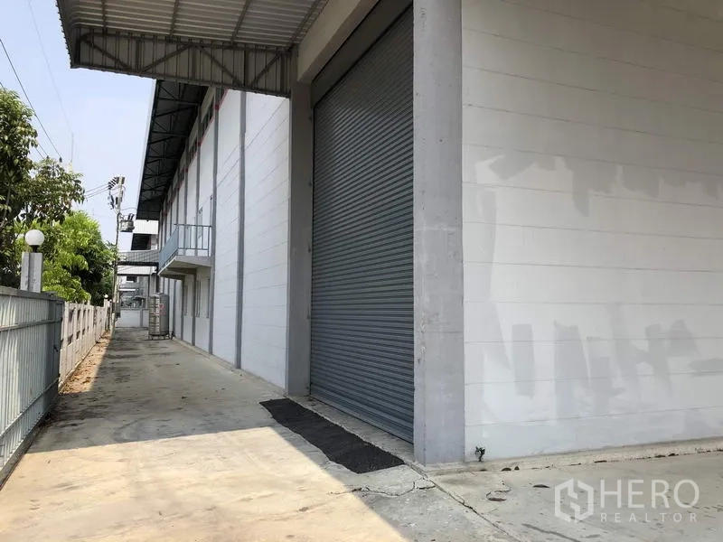 Factory for rent in Lam Luk Ka, Pathum Thani - Long side loading area with large roller shutter, canopy cover and security fence.