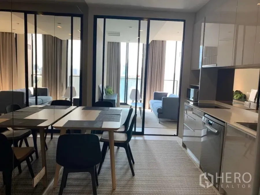 Condominium for rent in Pathum Wan, Bangkok - Open-plan dining area and glossy kitchen with sliding glass doors to a bright living room.