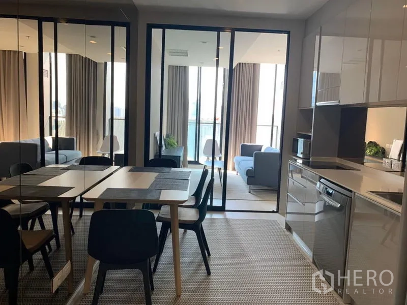Condominium for rent in Pathum Wan, Bangkok - Open-plan dining area and glossy kitchen with sliding glass doors to a bright living room.