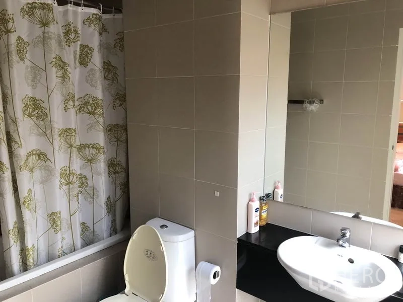 Townhouse for rent or sale in Suan Luang, Bangkok - Bathroom with bathtub and patterned shower curtain, toilet, wide mirror and vanity.