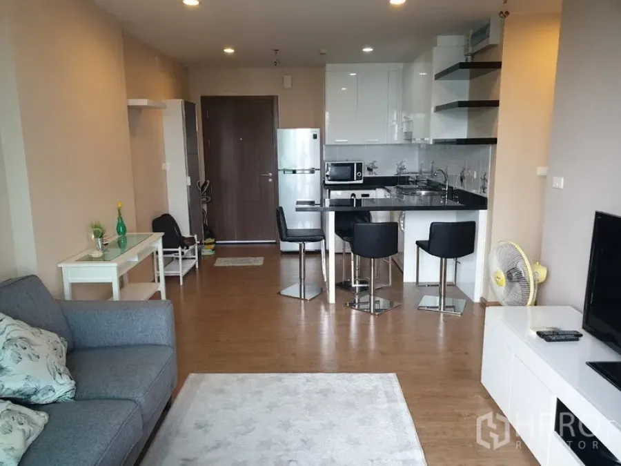 Condominium for rent in Watthana, Bangkok - Open-plan living room with sofa, TV console and modern kitchen with breakfast bar.