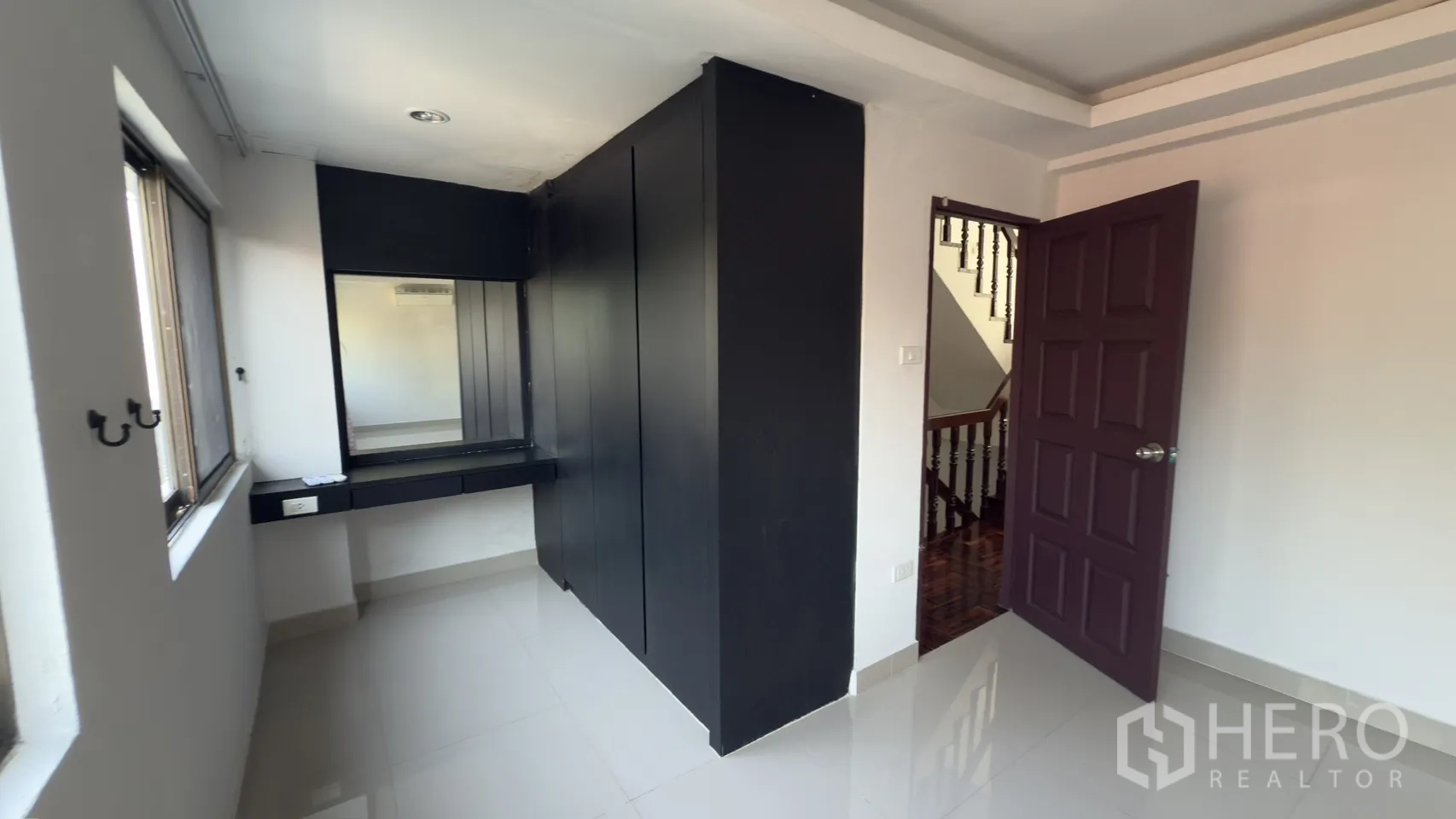 Townhouse for rent in Watthana, Bangkok - Bright room with glossy tile floor, a large black wardrobe and built-in dressing table beside the staircase.