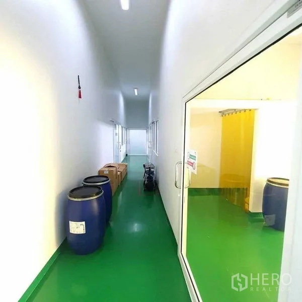Factory for sale in Bang Pa-in, Phra Nakhon Si Ayutthaya - Bright hallway with blue drums, boxes and access to a yellow-curtained room.