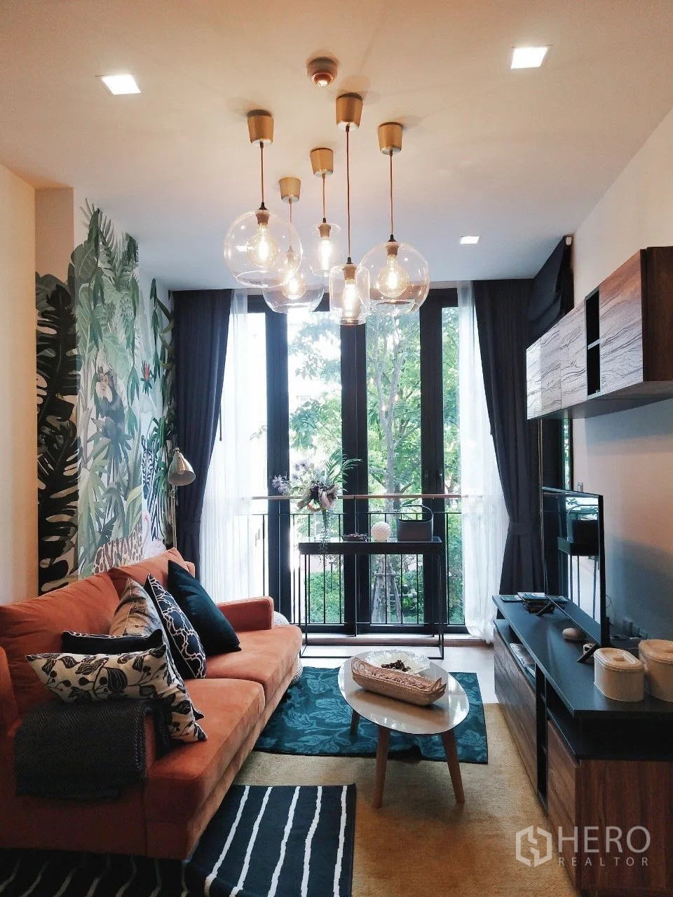 Condominium for rent in Watthana, Bangkok - Inviting lounge with globe pendant lights, sofa, and a green garden outlook.