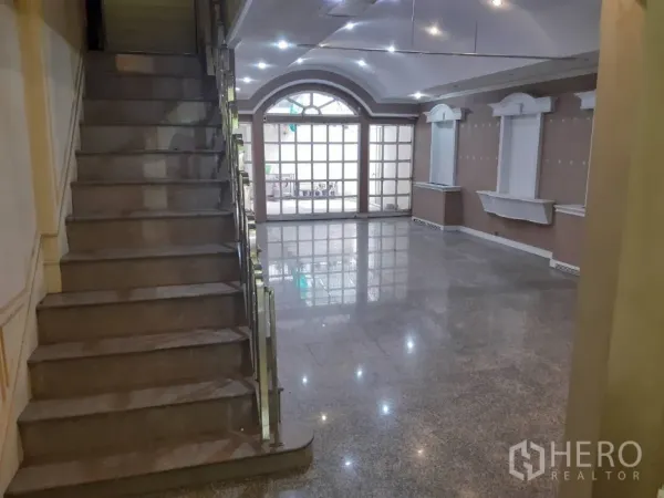 Townhouse for rent in Khlong Toei, Bangkok - Open‑plan lounge featuring a staircase, recessed lighting and large glass doors.