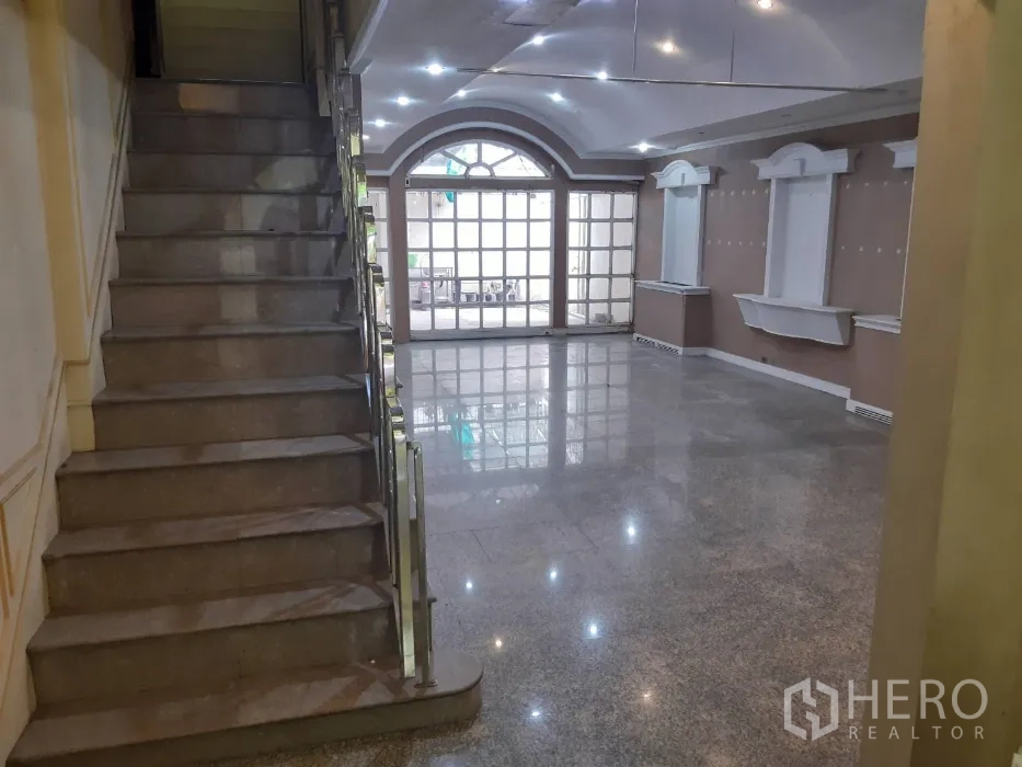 Townhouse for rent in Khlong Toei, Bangkok - Open‑plan lounge featuring a staircase, recessed lighting and large glass doors.