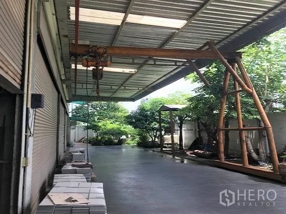 工厂 出售在Khlong Luang, Pathum Thani - 带顶装卸区，混凝土地面，龙门起重滑车与边侧绿树。