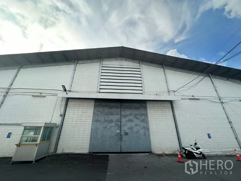货栈 出租在Khlong Toei, Bangkok - 仓库外立面设大型金属对开门、通风百叶和小型警卫亭。