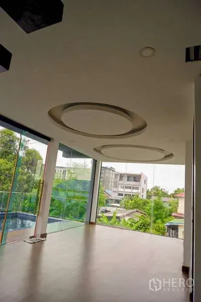 Detached House for sale in Lat Phrao, Bangkok - Bright living area with circular recessed ceilings and floor-to-ceiling windows overlooking greenery.