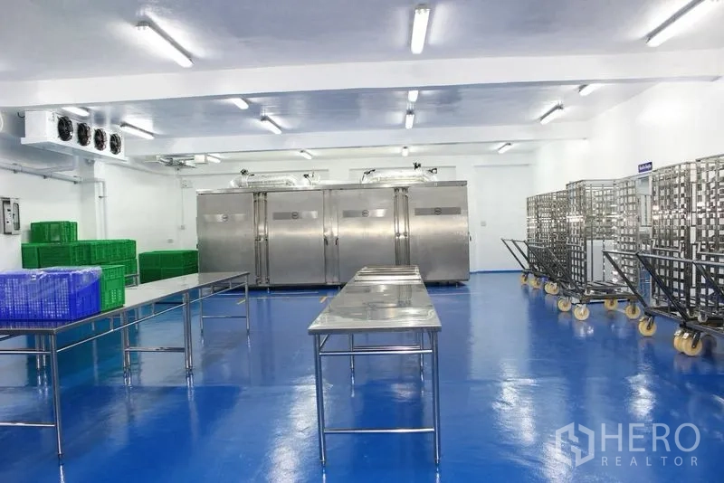 Factory for rent or sale in Krathum Baen, Samut Sakhon - Large clean hall with stainless chambers, blue floor, and plastic crates on the sides.
