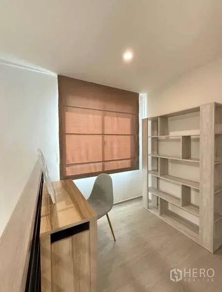 Townhouse for rent in Bang Phli, Samut Prakan - Compact study room with wooden desk, gray chair and shelving, brown Roman blinds.