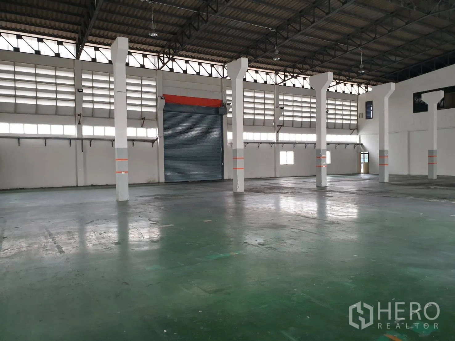 Factory for rent in Bang Pakong, Chachoengsao - Open factory floor with smooth concrete surface, white pillars, louvered windows and a large roller shutter door.