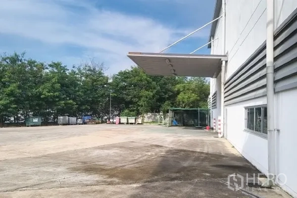Factory for sale in Rayong - Spacious concrete yard beside the factory with canopy and trees at the boundary.