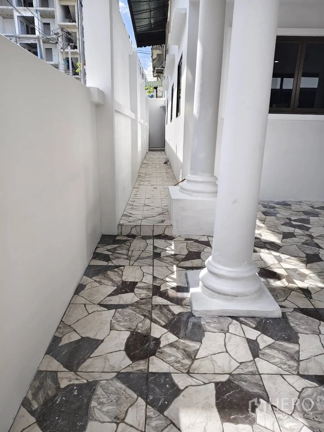 Townhouse for sale in Phra Khanong, Bangkok - Side walkway along the house with columns and patterned floor tiles.