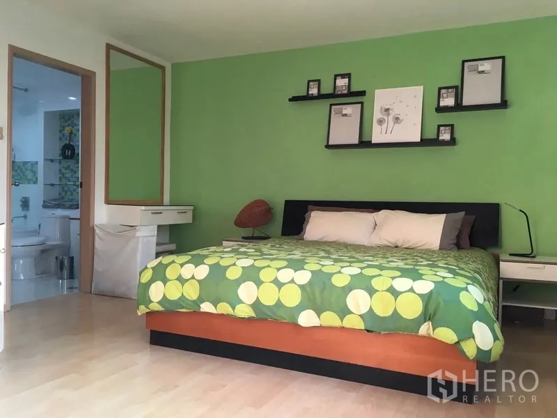 Condominium for rent in Pathum Wan, Bangkok - Master bedroom with green accent wall, king bed, floating shelves, and doorway to the bathroom.