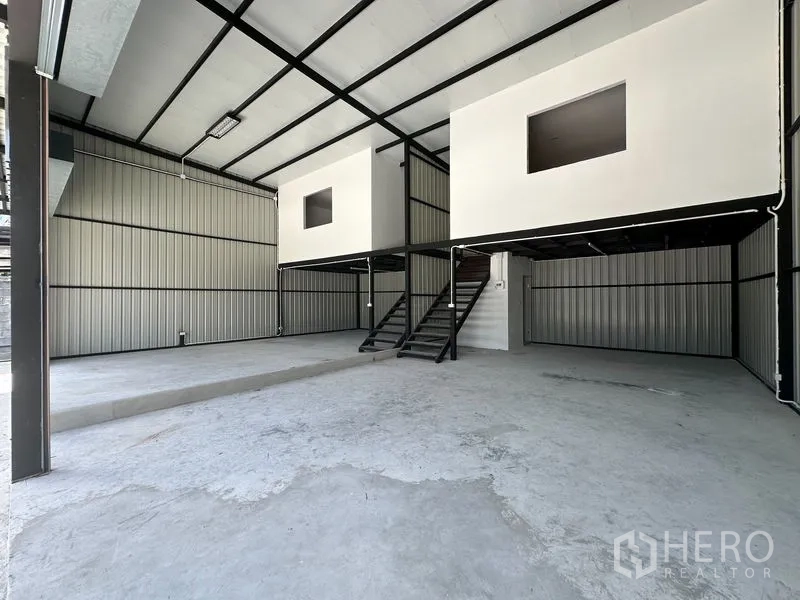 Warehouse for rent - High-ceiling warehouse interior with steel frame, concrete floor, and mezzanine office rooms accessed by stairs.