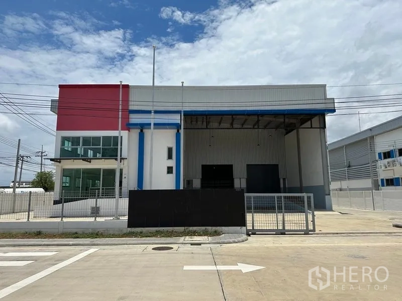 Factory for rent in Mueang Samut Prakan, Samut Prakan - Modern factory exterior with gated entrance, office wing and covered loading bays on a clear day.