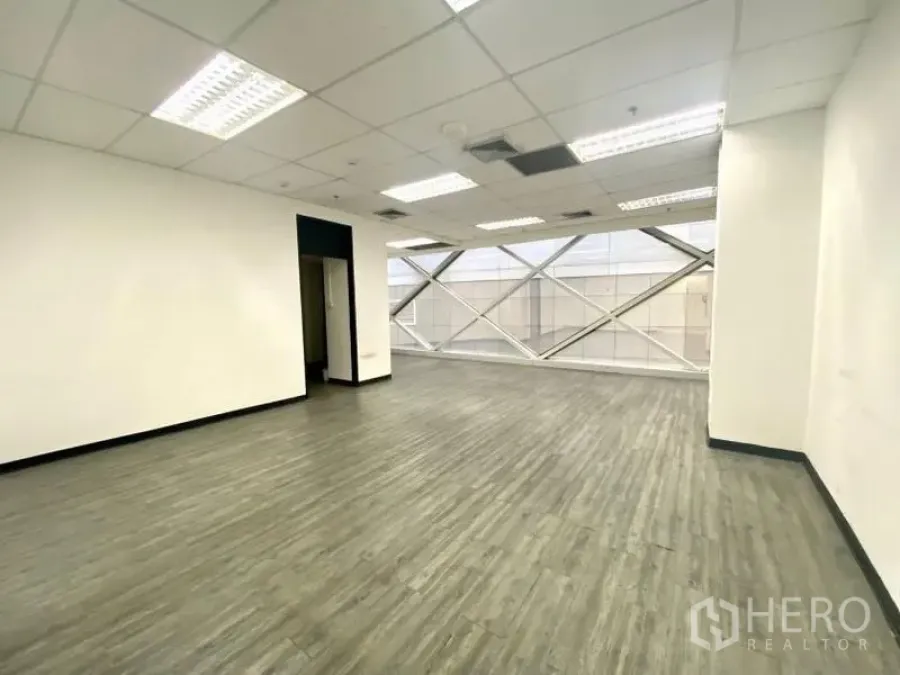 Office Space for rent in Khlong Toei, Bangkok - Bright open-plan office with wood-look vinyl flooring, white walls, grid ceiling, and large diagonal-braced window.