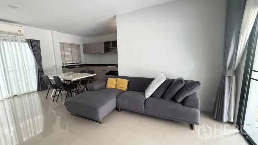 Townhouse for rent in Bang Phli, Samut Prakan - Living and dining space with a gray sectional sofa and glossy tiled floor.