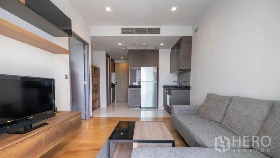 Condominium for rent or sale in Khlong Toei, Bangkok - Open living room facing a built-in TV console and full kitchen with stainless refrigerator.