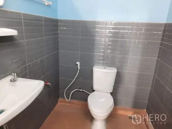 Warehouse for rent in Khlong Luang, Pathum Thani - Clean tiled restroom inside the warehouse featuring toilet, handheld bidet and sink.
