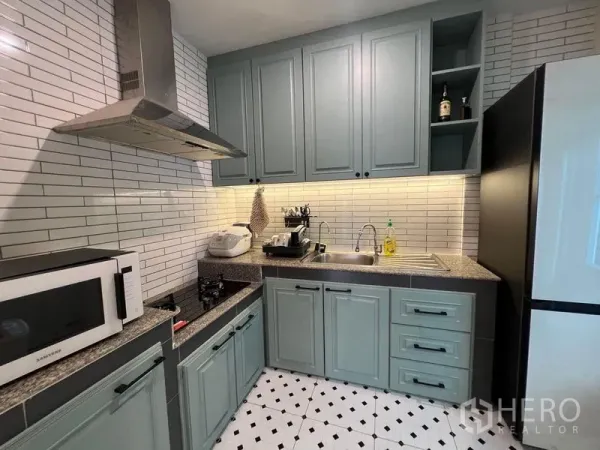 Detached House for sale in Bang Kruai, Nonthaburi - Compact L‑shaped kitchen with grey‑blue cabinetry, range hood, tiled backsplash and appliances.