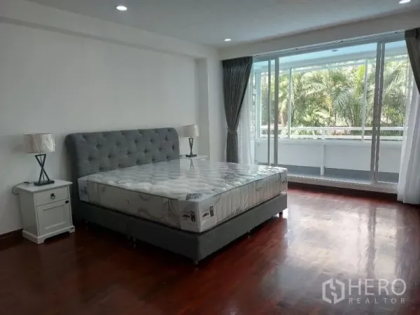 Condominium for rent in Watthana, Bangkok - Bright bedroom with tufted bed and large glass doors opening to a balcony with palm tree outlook.