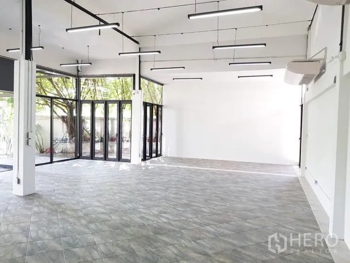 Office Space for rent in Chatuchak, Bangkok - Large open-plan room with glass corner walls and garden views beneath mature trees.
