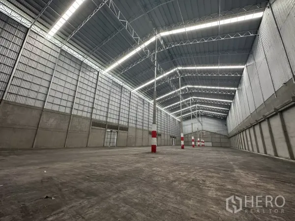 Warehouse for rent in Mueang Pathum Thani, Pathum Thani - Spacious high‑ceiling warehouse interior with steel truss roof, skylight strips and open floor area.