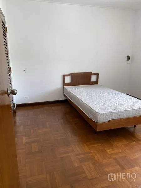 Apartment for rent in Khlong Toei, Bangkok - Second bedroom with wooden bed frame and mattress on parquet flooring and white walls.
