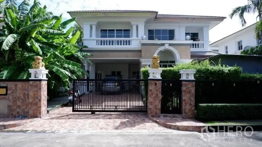 Detached House for rent in Prawet, Bangkok - Gated two-storey detached house with tiled driveway, carport and lush greenery in front.
