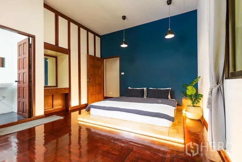 Townhouse for rent in Watthana, Bangkok - Primary bedroom with blue feature wall, platform bed and ensuite bathroom.
