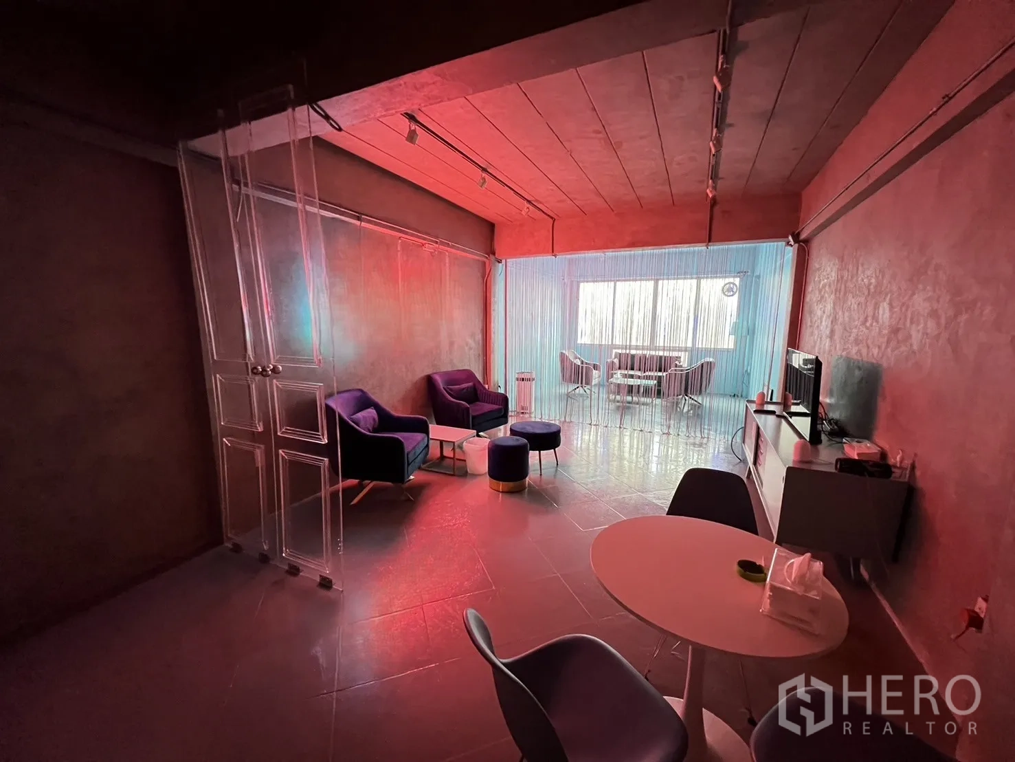 Shophouse for rent or sale in Watthana, Bangkok - Lounge area with soft seating and red ambient lighting divided by a string curtain.