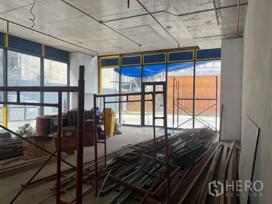 Retail Space for rent - Open-plan shell retail unit with high ceiling, floor-to-ceiling glass frontage, and scaffolding and materials inside.