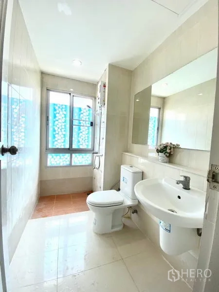 联排别墅 出租在Prawet, Bangkok - 浅色瓷砖浴室，设窗户、洗手台、坐便器与淋浴热水器。