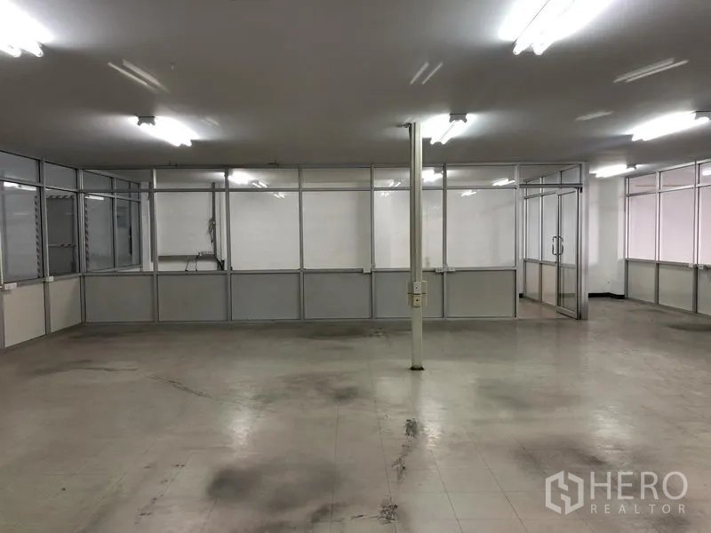 Warehouse for rent in Nonthaburi - Glass-partition office area inside the warehouse with fluorescent lighting and tiled flooring.